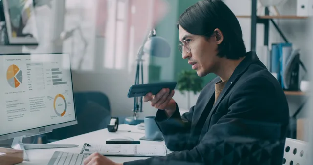 Business professional analyzing data charts on a computer while speaking on phone in an office setting. Employer branding: hvordan udvikler man et troværdigt arbejdsgiverbrand?